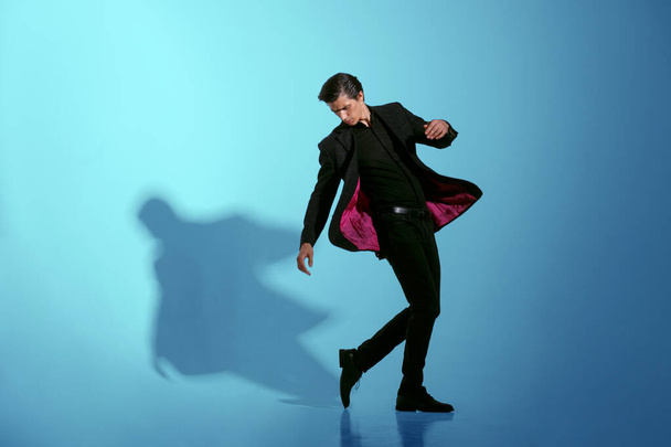 Движущее изображение привлекательного сильного молодого человека в полностью элегантном черном костюме, изолированном на синем фоне. Копирование пространства. - Фото, изображение