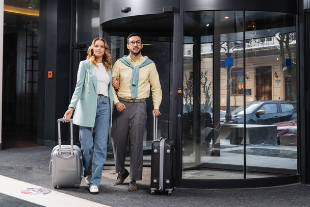 Дрожащая межрасовая пара с мешочком стоит у дверей отеля  - Фото, изображение