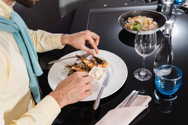 Vue recadrée de l'homme assis près de délicieuses crevettes sur l'assiette dans la chambre d'hôtel  - Photo, image