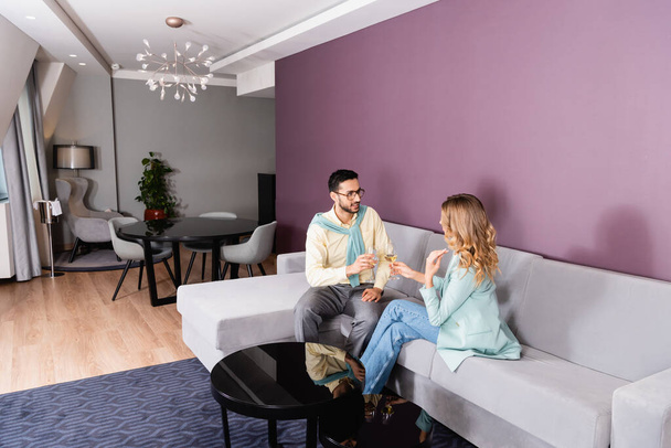 Araber hält Glas Wein neben Freundin auf Couch im Hotel  - Foto, Bild