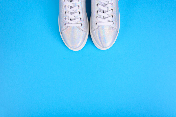 Silver sneakers on a blue background with place for text. Studio Photo - Photo, Image