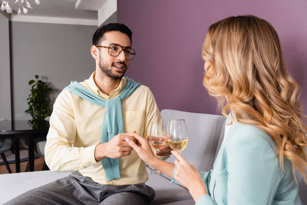 Muslim man with glass of wine holding hand of girlfriend in hotel room  - Fotó, kép