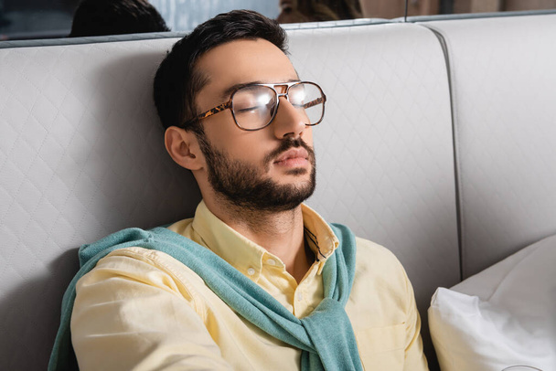 Muslim man in eyeglasses sitting on bed in hotel  - 写真・画像