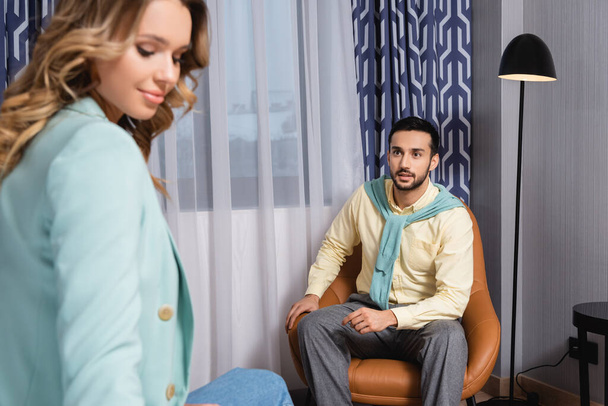 Hombre árabe mirando a su novia en primer plano borroso mientras está sentado en el sillón  - Foto, Imagen