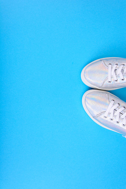 Zapatillas de deporte de plata sobre un fondo azul con lugar para el texto. Estudio foto - Foto, imagen