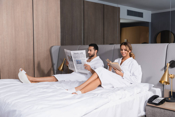 Sorrindo mulher ler livro perto namorado árabe com jornal no hotel  - Foto, Imagem