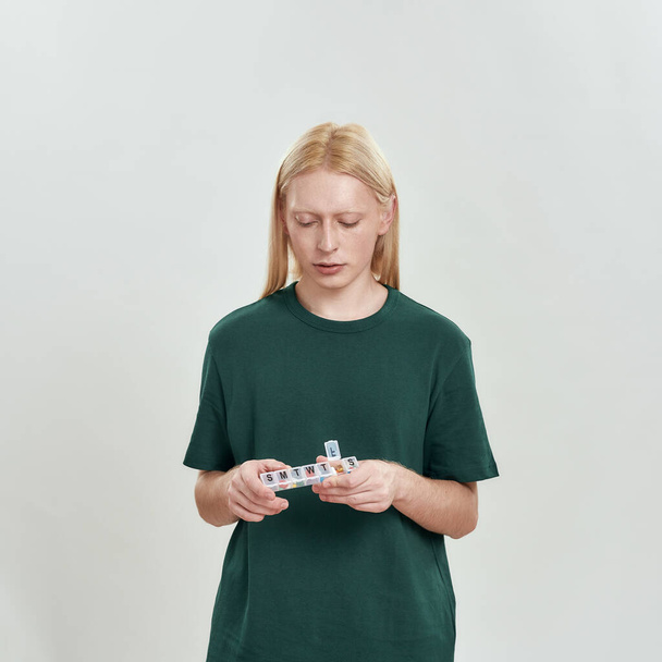 Молодий білий чоловік дивиться на організатора таблеток в руках
 - Фото, зображення
