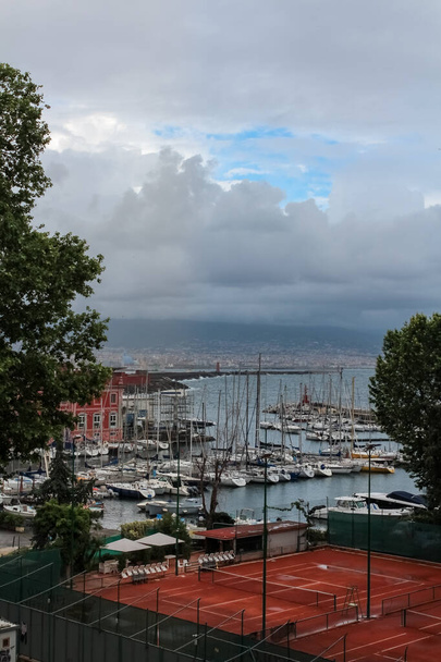 Άποψη άδειου γηπέδου τένις και ιστιοφόρων αγκυροβολημένων σε λιμάνι της Νάπολης, Ιταλία. - Φωτογραφία, εικόνα