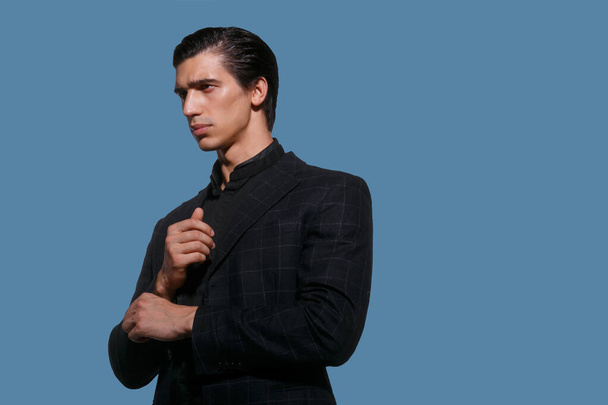 Business portrait of a handsome fit young man in black suit arrange her sleeve, over blue background. Horizontal view. - Foto, afbeelding