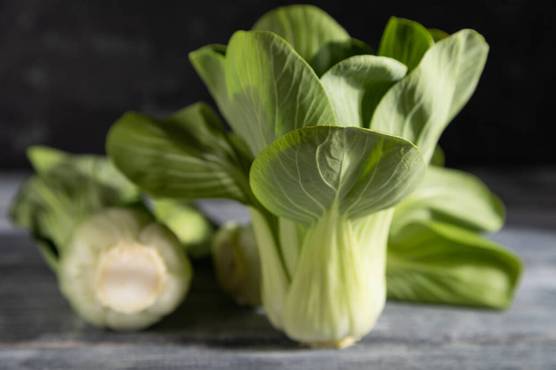 Fresh green bok choy or pac choi chinese cabbage on a gray wooden background. Hard light, contrast, dark, moody. Side view, close up, selective focus. - Valokuva, kuva