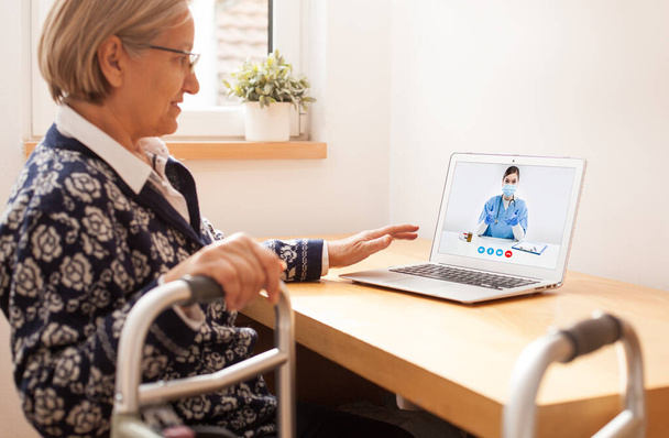高齢者の高齢者の高齢者の女性は、仮想遠隔医療ビデオ通話を介して英国NHS GP女性医師と話をモビリティ問題を持ちます,歩行フレームを保持します,オンライン予約治療,テレヘルスコンセプト - 写真・画像