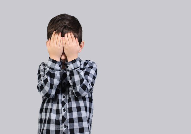 Ongelukkige schooljongen, 6-jarige jongen bedekte zijn gezicht met zijn handen op studio grijs geïsoleerde achtergrond.Wraakzuchtige jongen - Foto, afbeelding