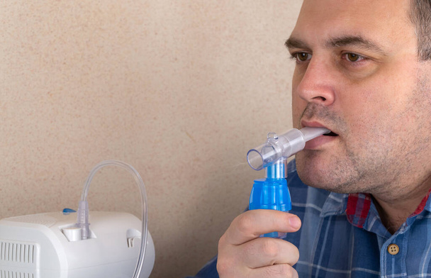 Ο άνθρωπος κάνει εισπνοές με τη βοήθεια νεφελοποιητή. Ο ασθενής αναπνέει με μάσκα οξυγόνου. συσκευή νεφελοποίησης μιας φαρμακευτικής ουσίας. χρησιμοποιείται στη θεραπεία του βρογχικού άσθματος και του αναπνευστικού - Φωτογραφία, εικόνα