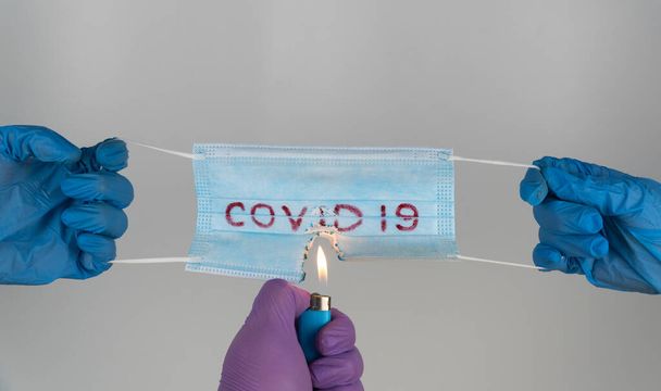 Üzerinde "covid-19" yazan tıbbi maske ateşle yanıyor. Cerrahi maskeyi yakar, solunum cihazlarını patlatırız..  - Fotoğraf, Görsel