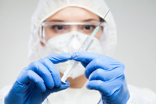 Női tudós kezében fecskendő és tű, visel védő laboratóriumi ruha, kesztyű, maszk, szemüveg, COVID-19 vakcina illusztráció, gyógymód és kezelés a globális Coronavirus járvány koncepció - Fotó, kép