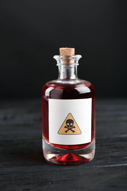 Glass bottle of poison with warning sign on black wooden table - Zdjęcie, obraz