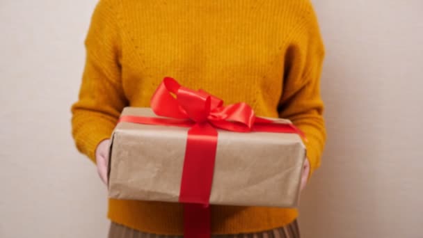 Unrecognizable woman in a mustard suite gives a gift wrapped in kraft paper and tied with a red ribbon - Footage, Video