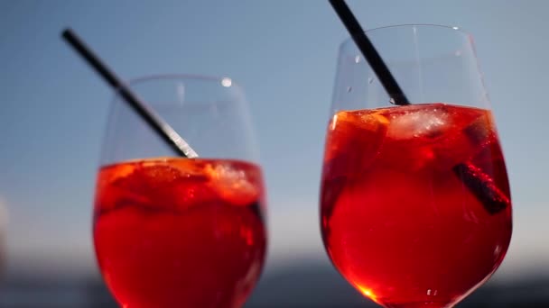 A glass of cocktail.Juicy delicious drink.red cocktail with ice with lemon slices in a glass with a straw on a background of blue sky - Footage, Video