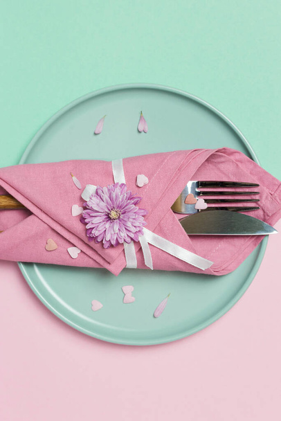 Bella tavola festiva con piatto verde, tovagliolo, fiori e cuori decorazione su sfondo rosa pastello e verde. Vista dall'alto con spazio di copia. - Foto, immagini