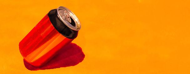 enfoque selectivo de una lata de refresco rojo y negro inclinada con fondo naranja - Foto, imagen