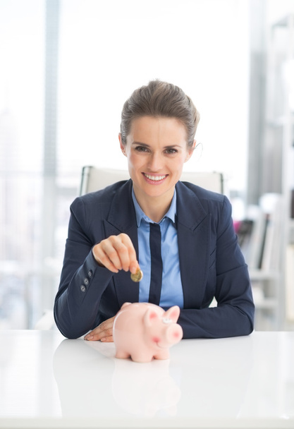 Business woman putting coin into piggy bank - Фото, изображение