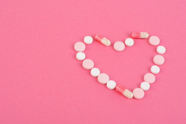Multicolored pills, capsules are laid out in the shape of a heart on a pink background. Heart diseases.Health care concept. - Valokuva, kuva