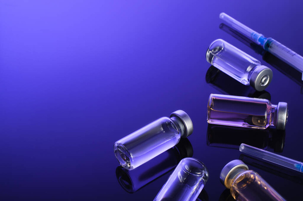 Шприцы, маленькие бутылочки, стеклянные флаконы с вакциной, лекарства на темно-синем фоне. Короновирусная вакцинация, клинические испытания вакцин, Медицинские исследования - Фото, изображение