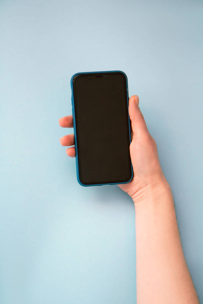 女性の手を握り、ライトブルーの背景にスマートフォン。モックアップ - 写真・画像