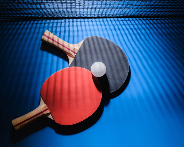 table tennis racket on a blue table with a ball. Beautiful light and shadow from the grid. Ping pong - Zdjęcie, obraz