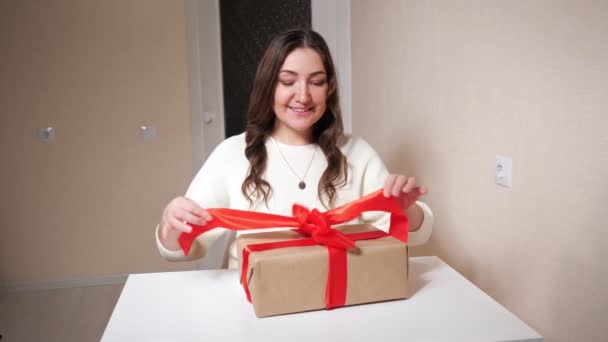 Belle femme brune déballonne un cadeau assis à la table - Séquence, vidéo