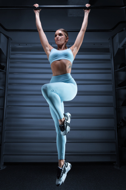 Atletica ragazza accosta sul bar in palestra su uno sfondo blu. Il concetto di sport, fitness, aerobica, bodybuilding, stretching. Mezzi misti - Foto, immagini