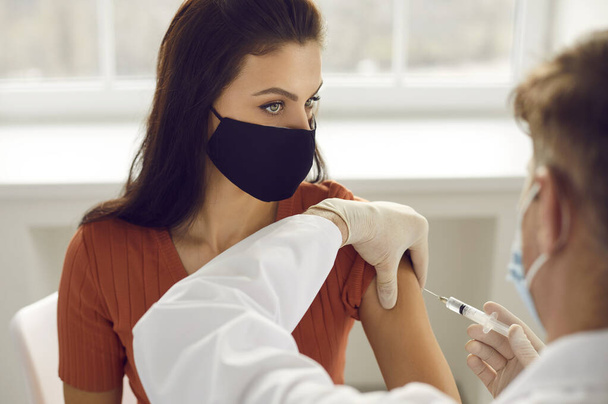 Woman in medical protective mask getting injection in arm vaccination against 19-ncov - Foto, imagen