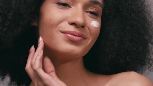 heureuse femme afro-américaine avec crème cosmétique sur le visage isolé sur gris - Séquence, vidéo
