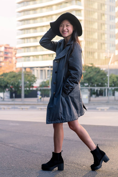 vertical photo of a happy and elegant asian woman in hat and trench coat walking downtown, urban lifestyle concept - Foto, Imagem