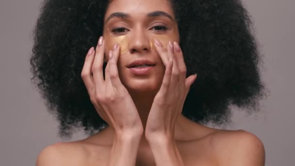 donna afro-americana che applica macchie oculari idrogel isolate sul grigio - Filmati, video