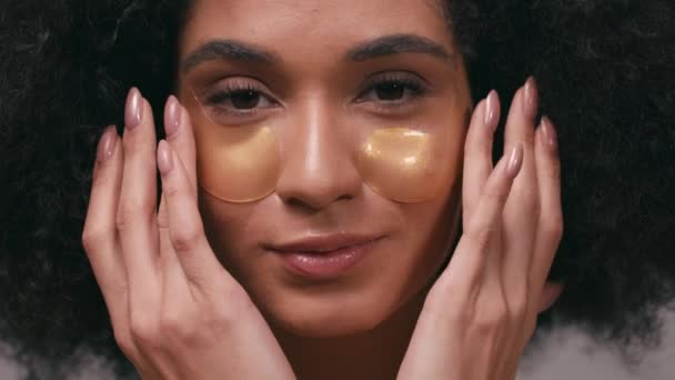vista da vicino della donna afro-americana che applica macchie oculari isolate sul grigio - Filmati, video