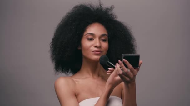 sorrindo mulher afro-americana aplicando pó facial isolado em cinza - Filmagem, Vídeo