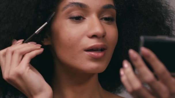 jeune femme afro-américaine brossant les sourcils isolé sur gris - Séquence, vidéo