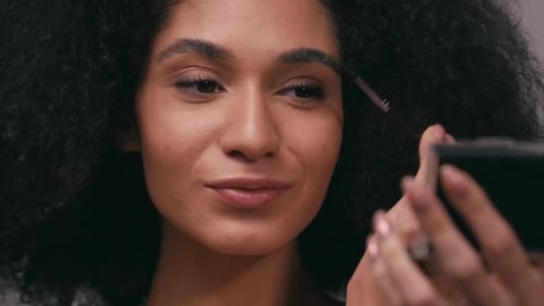 donna afro-americana sorridente che spazzola le sopracciglia isolate sul grigio - Filmati, video