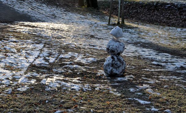 a snowman sadly slowly melting, dirty from mud and lack of snow will evoke a feeling of ruin and ugly changeable weather of winter February. frozen snow on lawn - Photo, Image