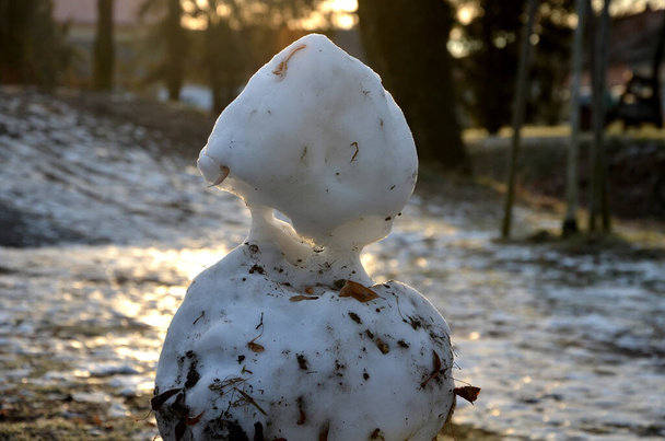 un muñeco de nieve lamentablemente se derrite lentamente, sucio por el barro y la falta de nieve evocará una sensación de ruina y feo clima cambiante del invierno de febrero. nieve congelada en el césped - Foto, imagen