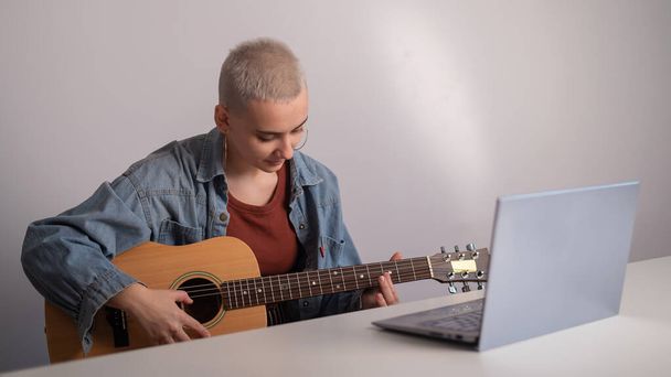 Młoda kobieta uczy się grać na gitarze online. Zdalne lekcje muzyki na laptopie - Zdjęcie, obraz