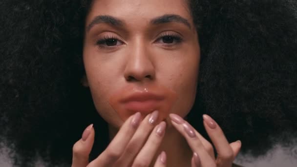 Kolajen dudak bandı yapıştıran genç Afrikalı Amerikalı kadın gri renkte izole edilmiş. - Video, Çekim