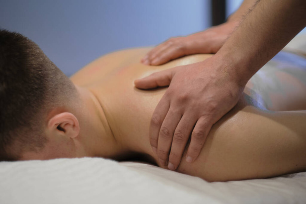 Nahaufnahme eines Mannes, der eine entspannende Schultermassage genießt. Mann entspannt sich auf Massagetisch bei Massage - Foto, Bild