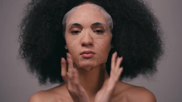 mujer afroamericana aplicando mascarilla hidratante aislada en gris - Metraje, vídeo