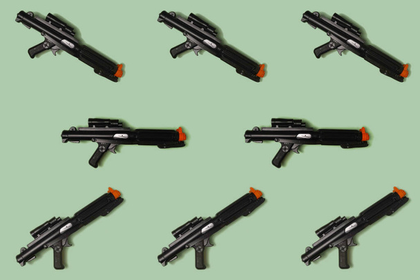 Pattern created of black rifle toys. A top view with pastel green background. - Photo, Image