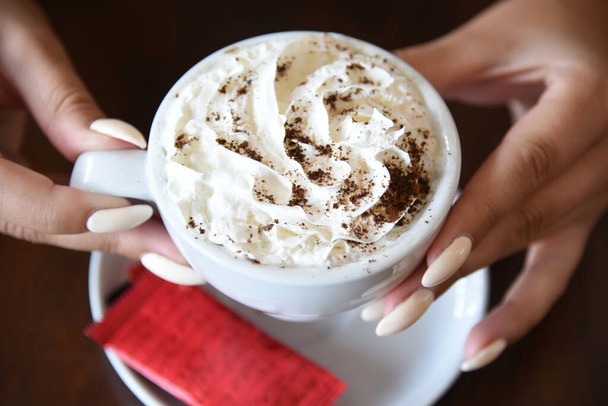 manos femeninas sosteniendo taza de café con crema batida - Foto, Imagen