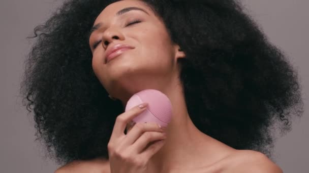 mujer afroamericana con los ojos cerrados usando limpiador de silicona aislado en gris - Metraje, vídeo
