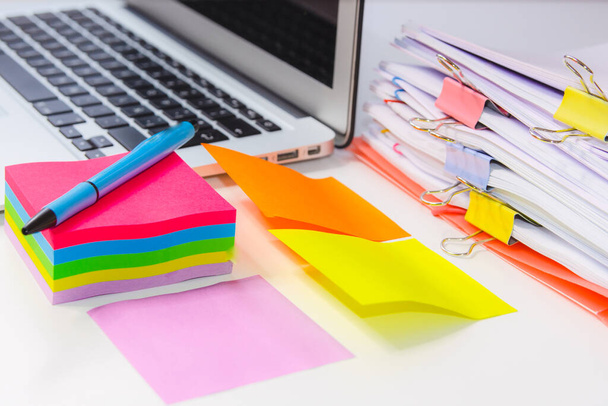 Nahaufnahme eines Papierstapels mit einem Notizbuch, farbigen Post-its und einem Stift. Konzept der Informationsüberlastung - Foto, Bild
