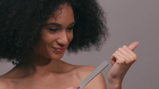 usmívající se africká americká žena dělat manikúru s pilníkem na nehty izolované na šedé - Záběry, video